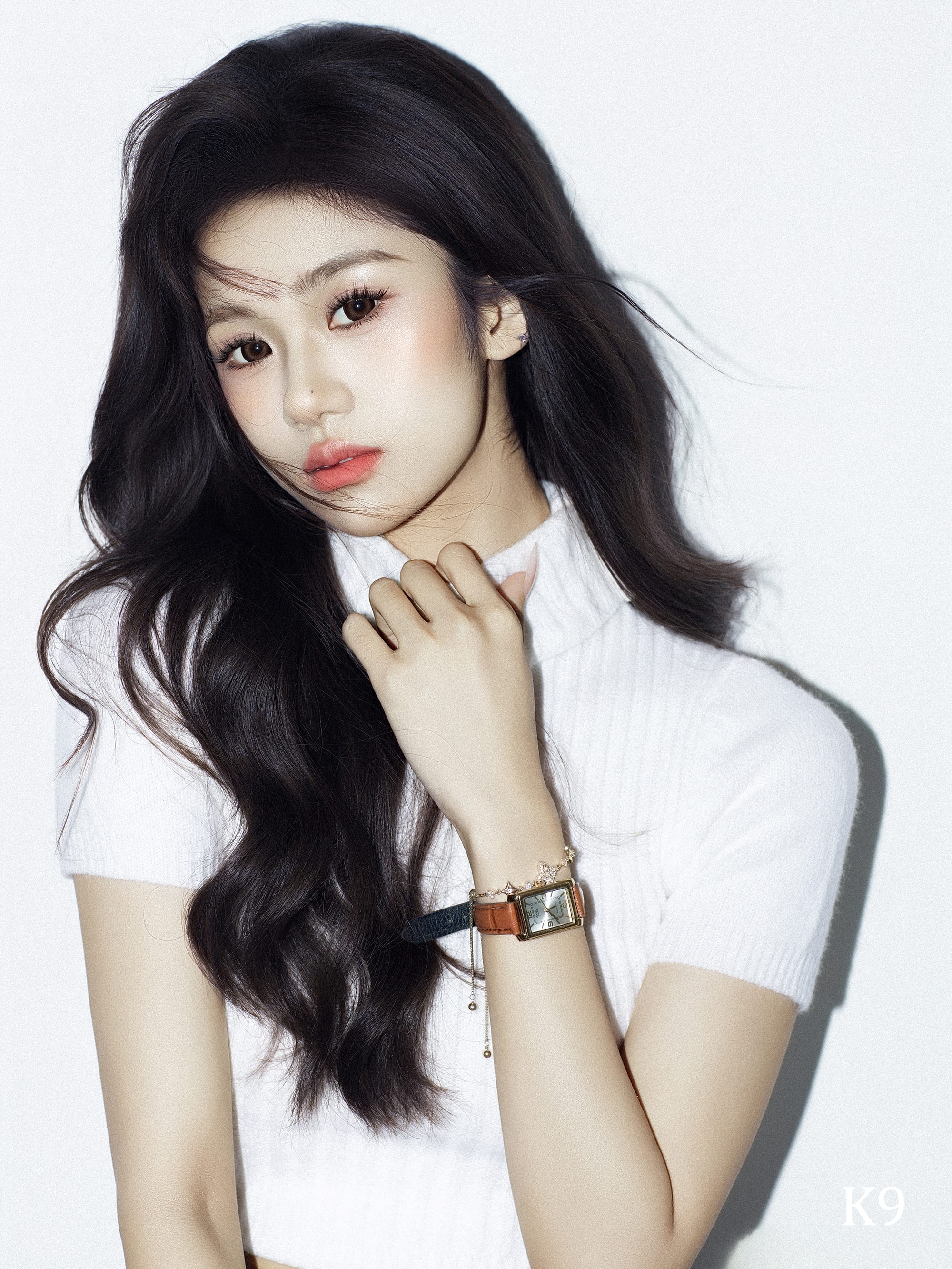 K9 Studio editorial portrait in a white ribbed top, gold watch and bracelet, wavy dark hair