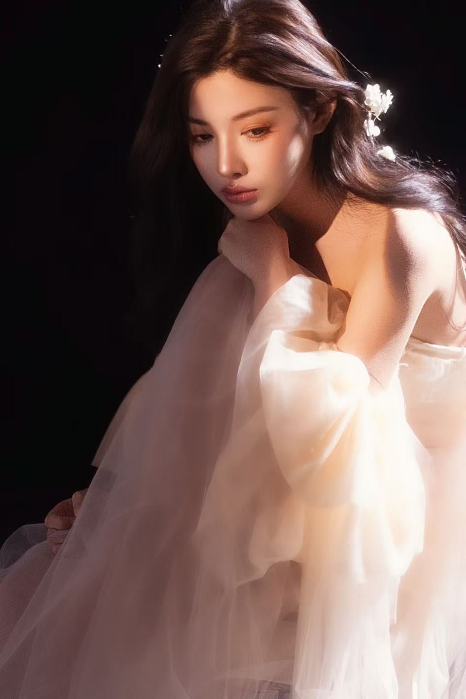 K9 Studio client portrait in a white tulle dress, hand near chin, floral hair accessory, dark background