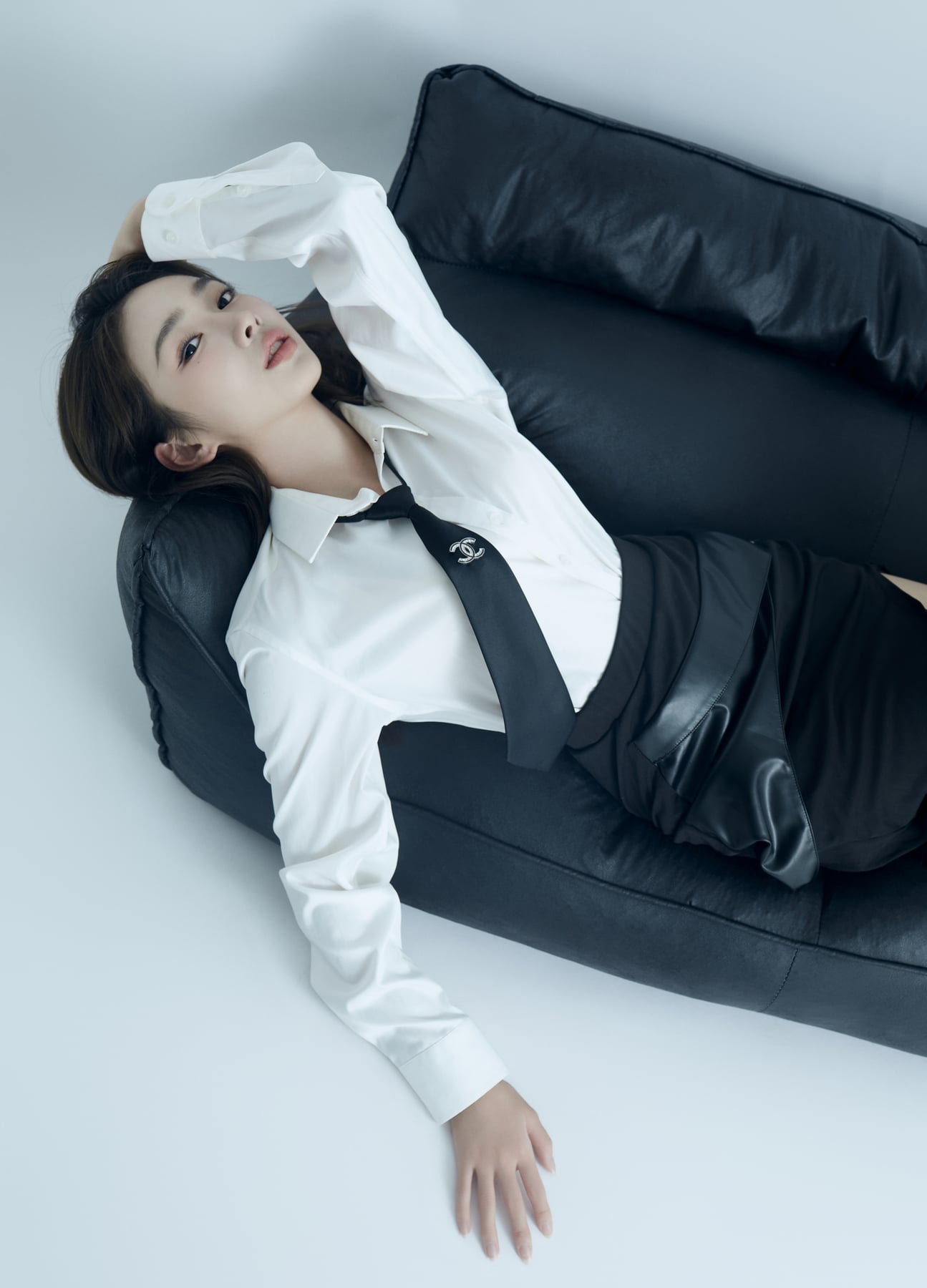 K9 Studio client portrait in a white shirt and black tie, leaning back on a black leather sofa, arm raised overhead