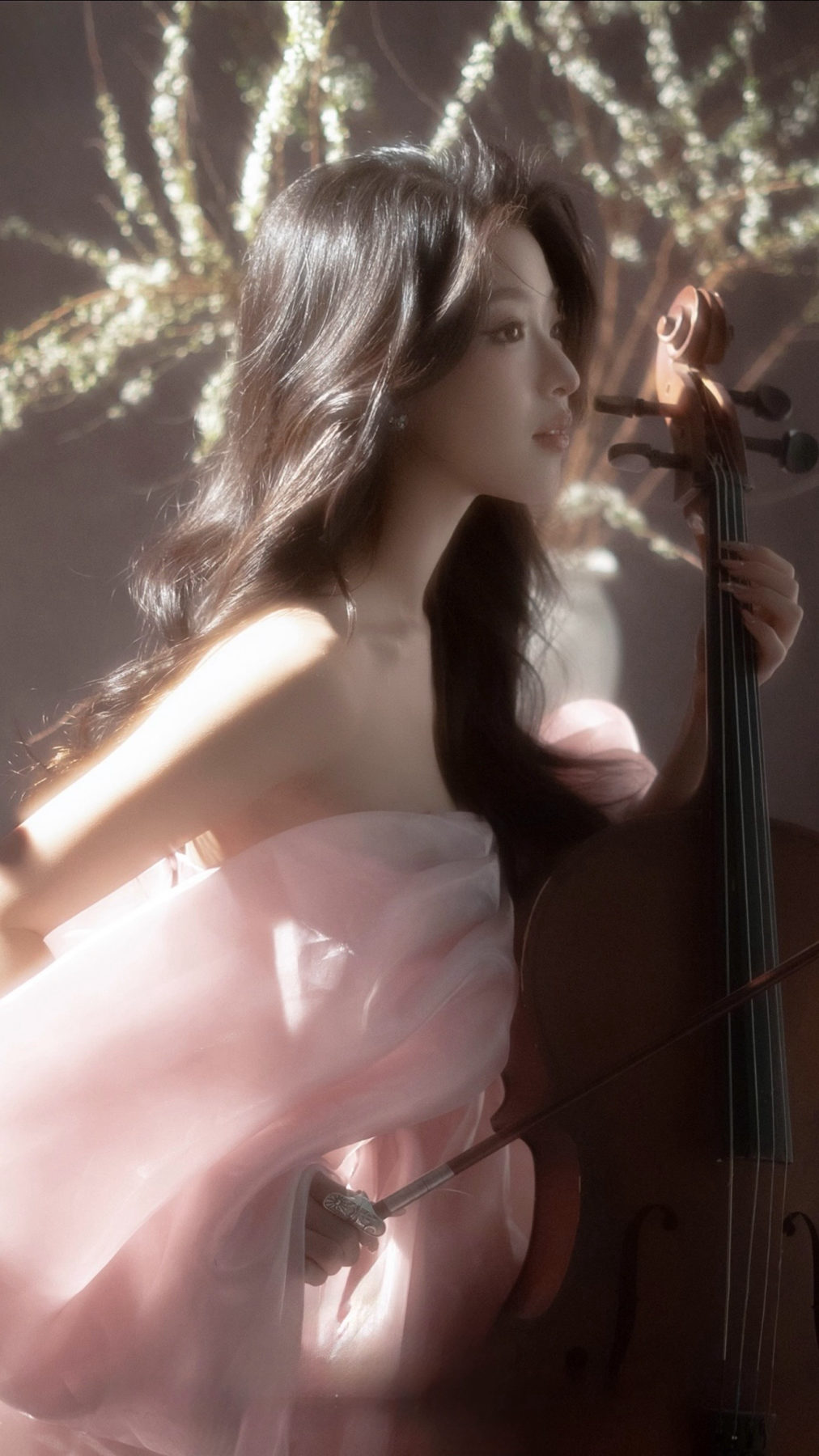 K9 Studio client portrait in a flowing pink gown holding a cello, dreamy blurred floral backdrop