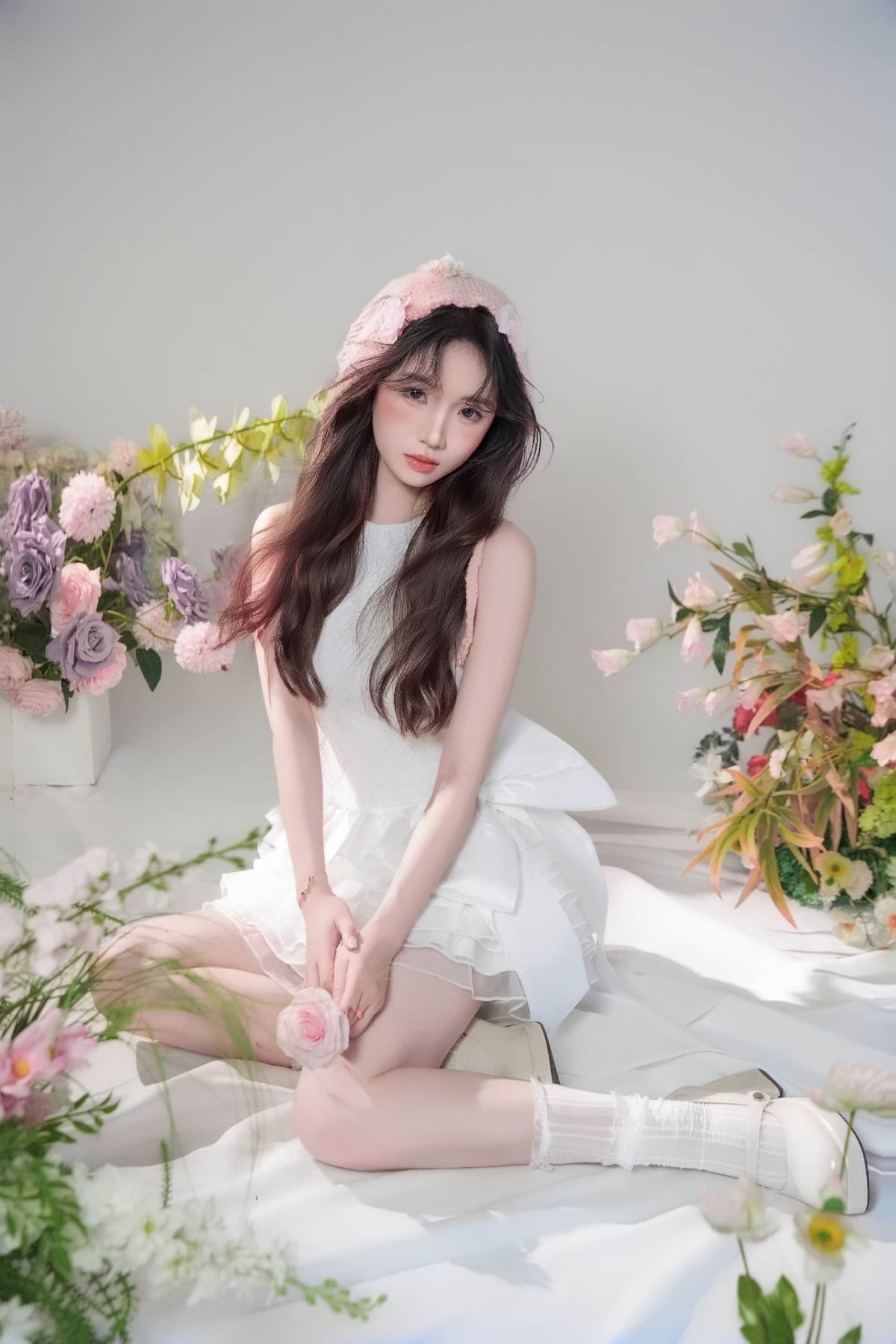 K9 Studio client portrait in a pink floral bonnet and white ruffled dress, kneeling among pastel florals