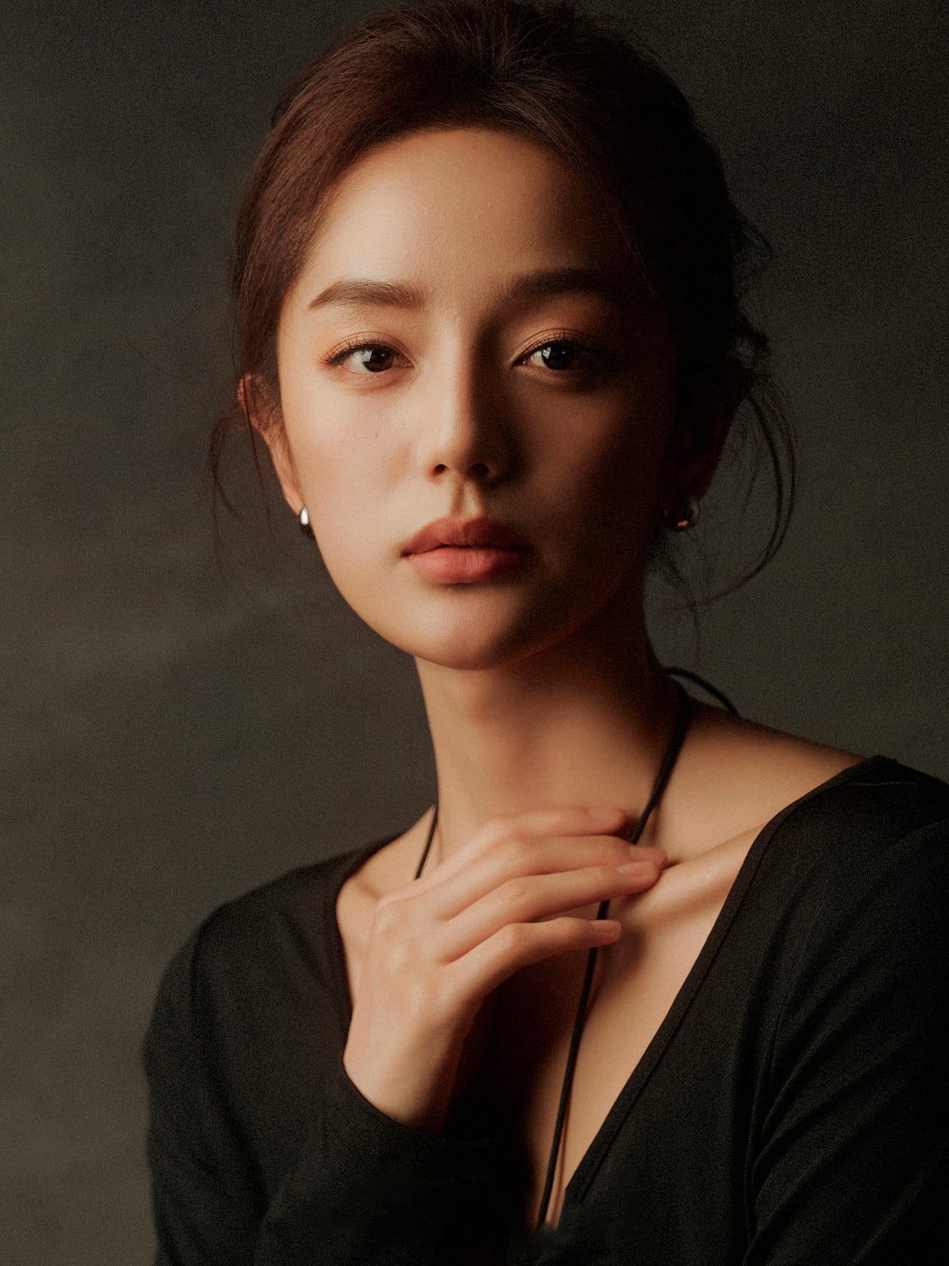 K9 Studio client portrait in a black v-neck top, moody low-key lighting, hand resting at the chest