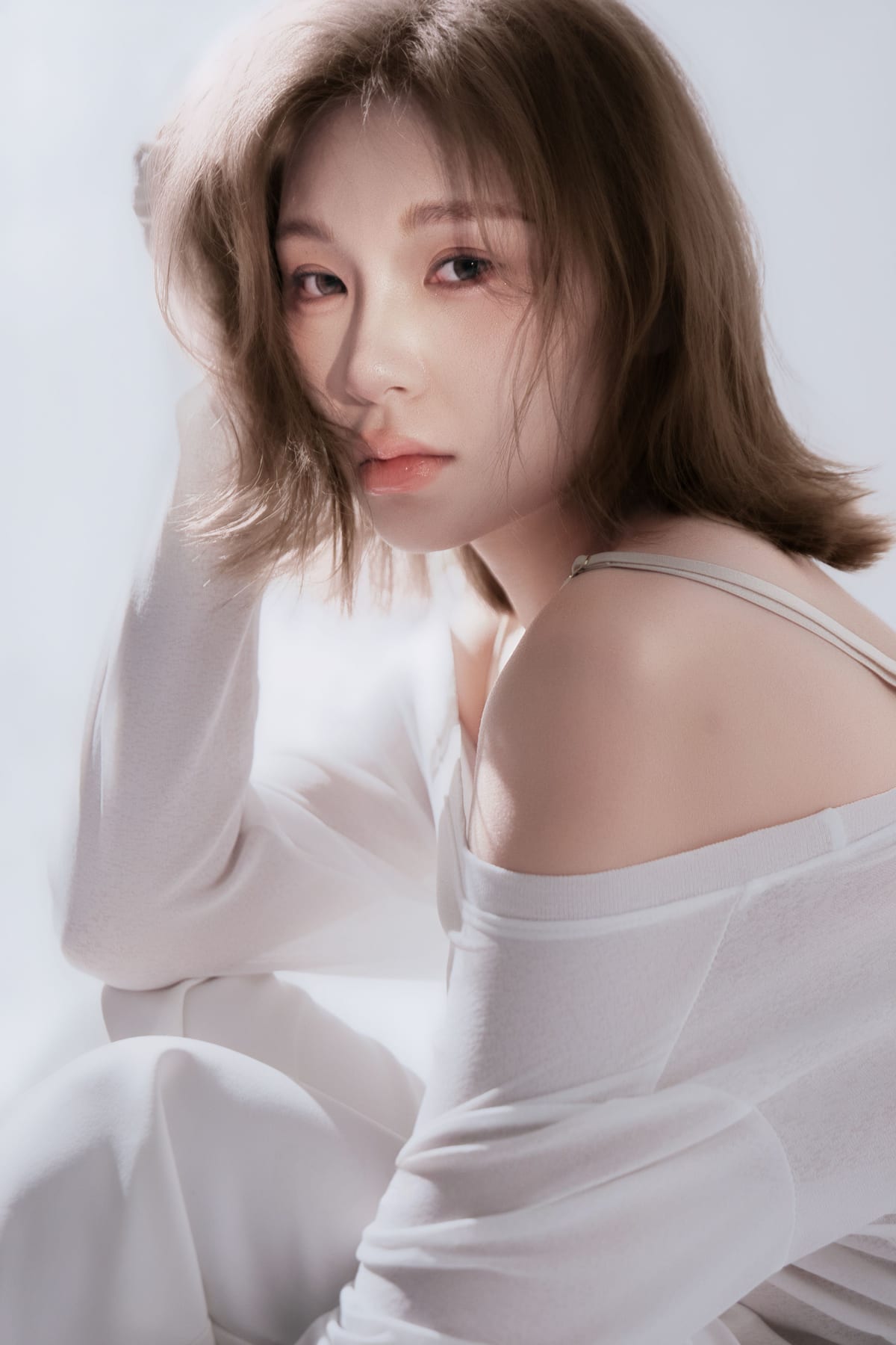 K9 Studio client portrait in a white off-shoulder top, soft diffused lighting, hand resting near the face